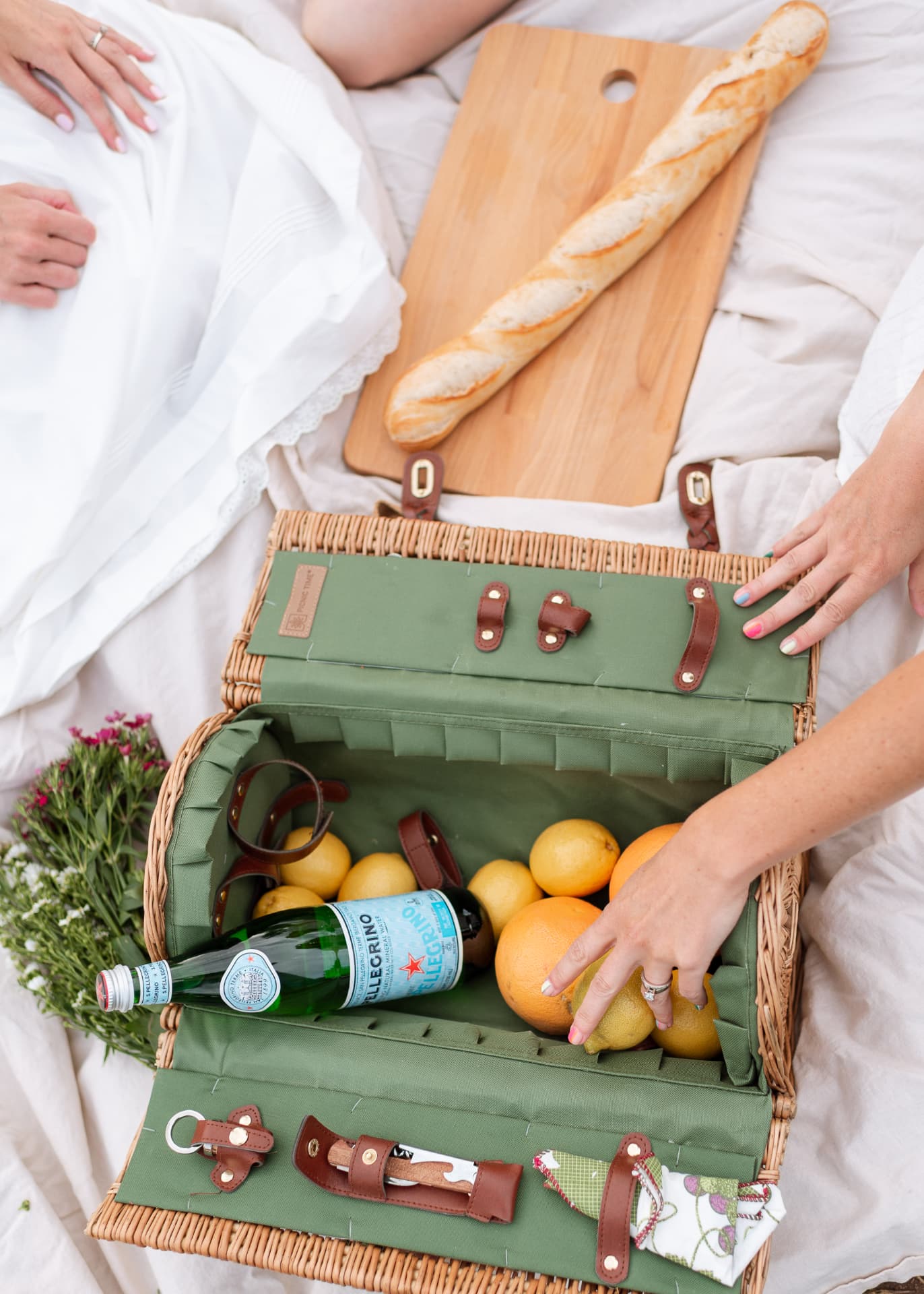 Open picnic basket with citrus, baguette and wildflowers