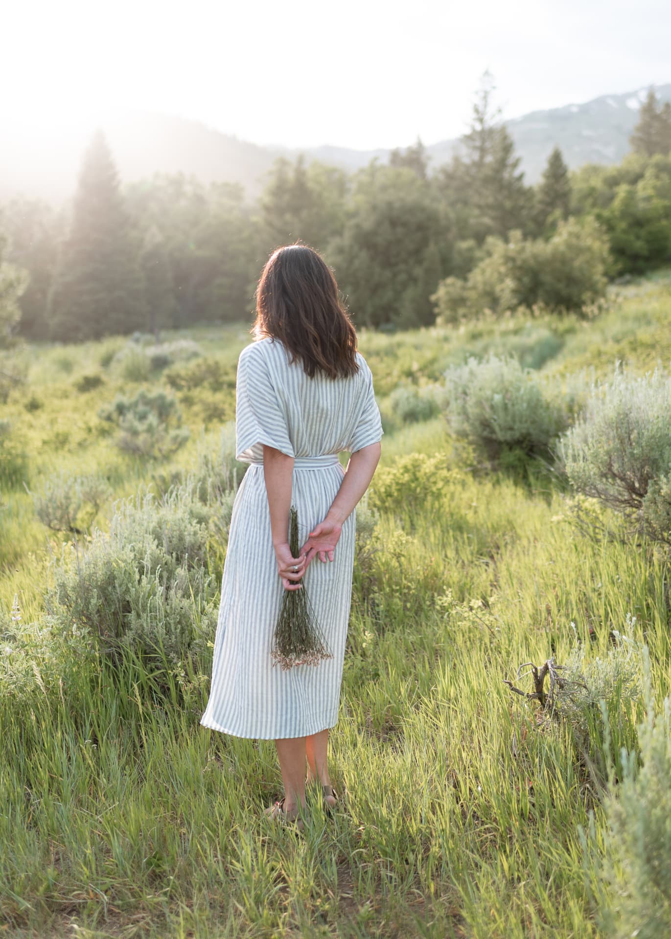 Woman in a striped linen dress holding wildflowers in a meadow