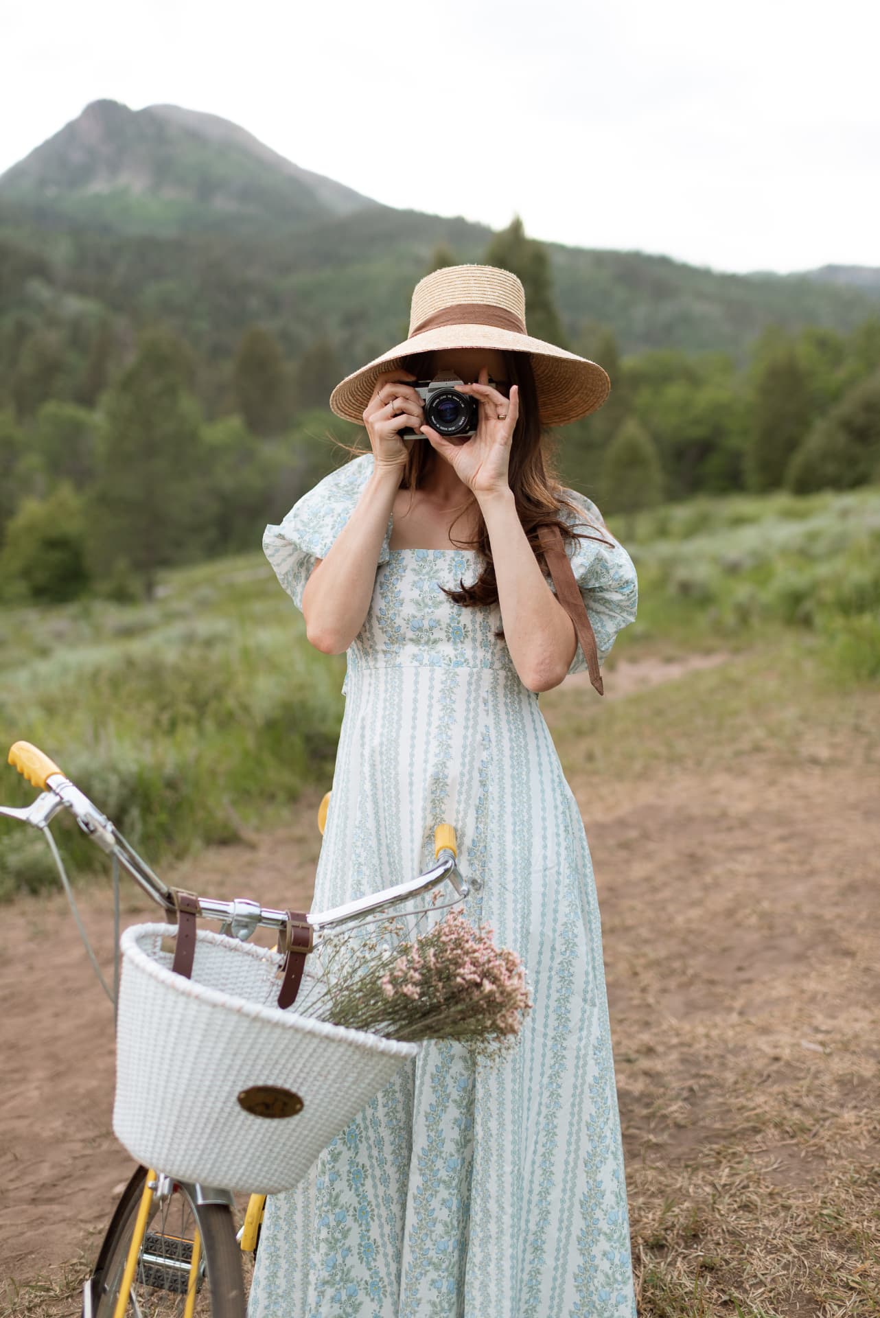 Woman in a blue floral dress with a straw hat and vintage camera