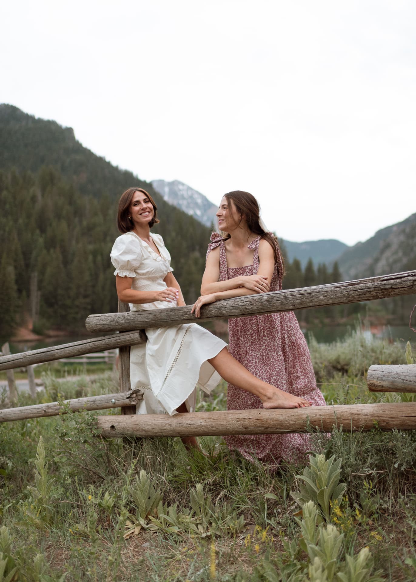 Two women resting on a rail fence by an alpine lake